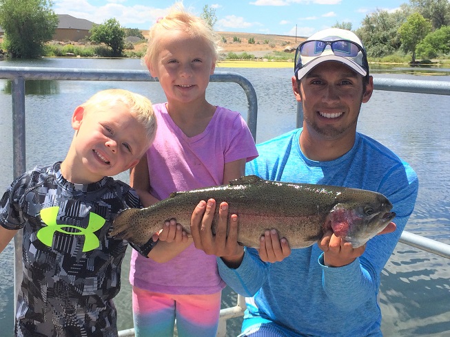 Young boy, young girl and Jordan Rodriguez posing with a huge rainbow trout