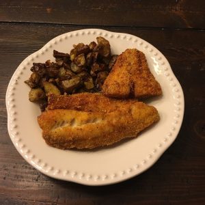 A plate featuring two fried fish fillets and roasted potatoes