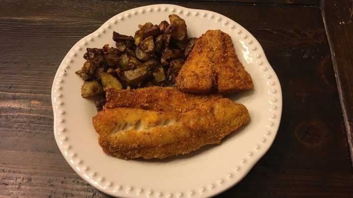 A plate featuring two fried fish fillets and roasted potatoes
