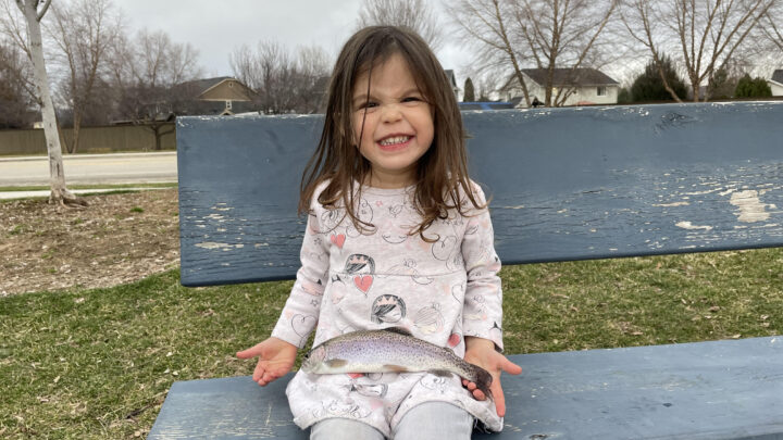 A young girl holds a rainbow trout caught in a local pond.