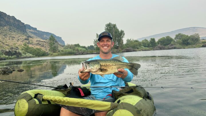 An angler with a largemouth bass caught while fishing from a float tube.