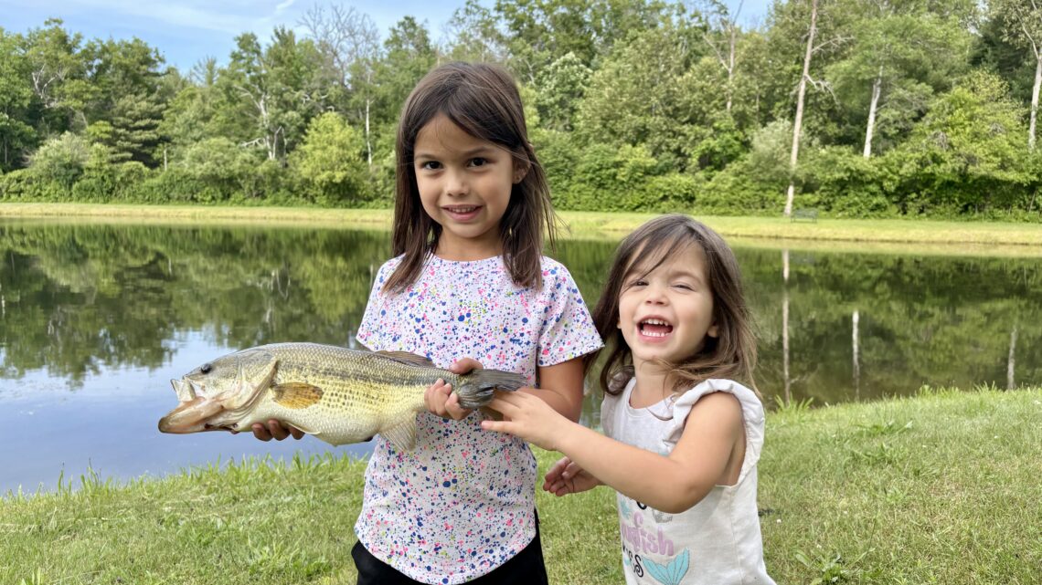 Two young girls holding a largemouth bass at a pond in northern Michigan.